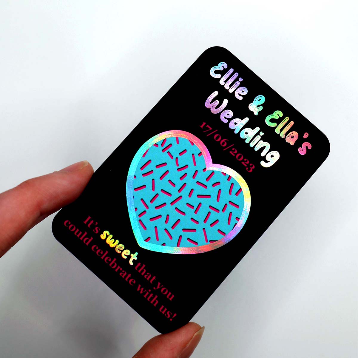 Holographic Ellie and Ella wedding save the date card with black rounded corner design, rainbow foil lettering, sprinkle heart illustration and pink wedding details.