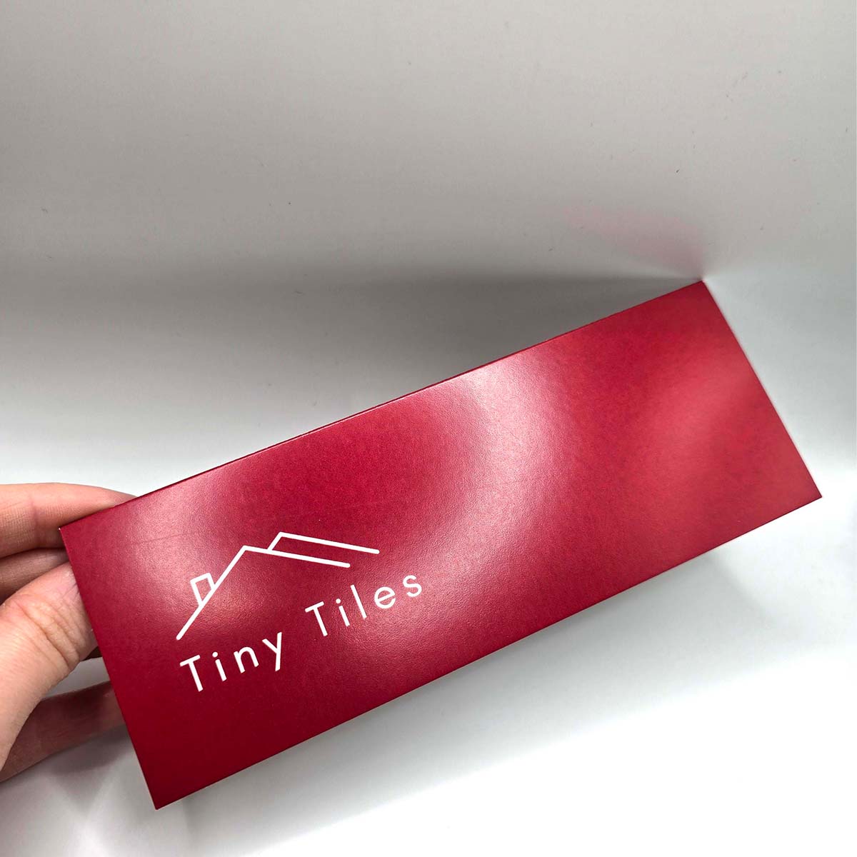 Small, red, folded header card for Tiny Tiles printed on silk stock with fine-line rooftop branding