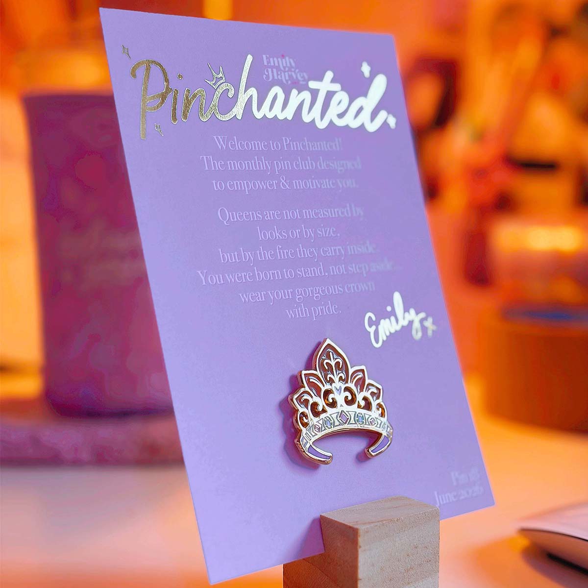 Metallic gold silk Pinchanted crown pin backing card with lavender design, white and gold foil lettering, and enamel crown pin attached.