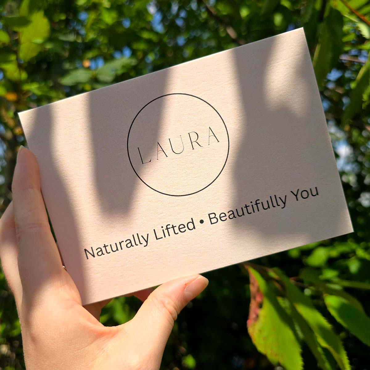 Gmund Cotton understated beauty postcard for Laura, featuring minimalist black typography on soft blush card, held outdoors in natural light.