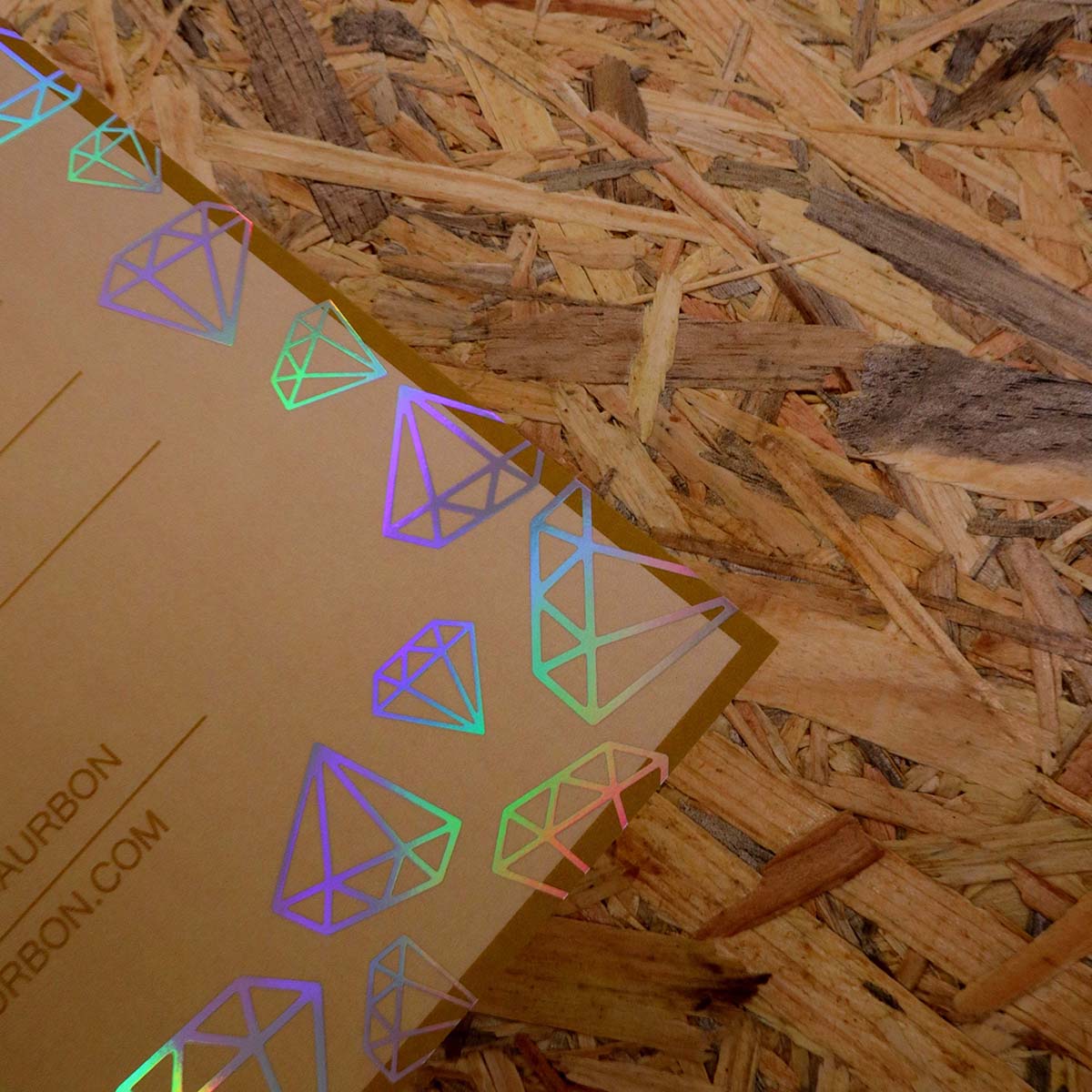 Close-up of a printed flyer featuring holographic foil diamond illustrations that shimmer in rainbow colours against a kraft brown background, showcasing reflective foil printing effects.