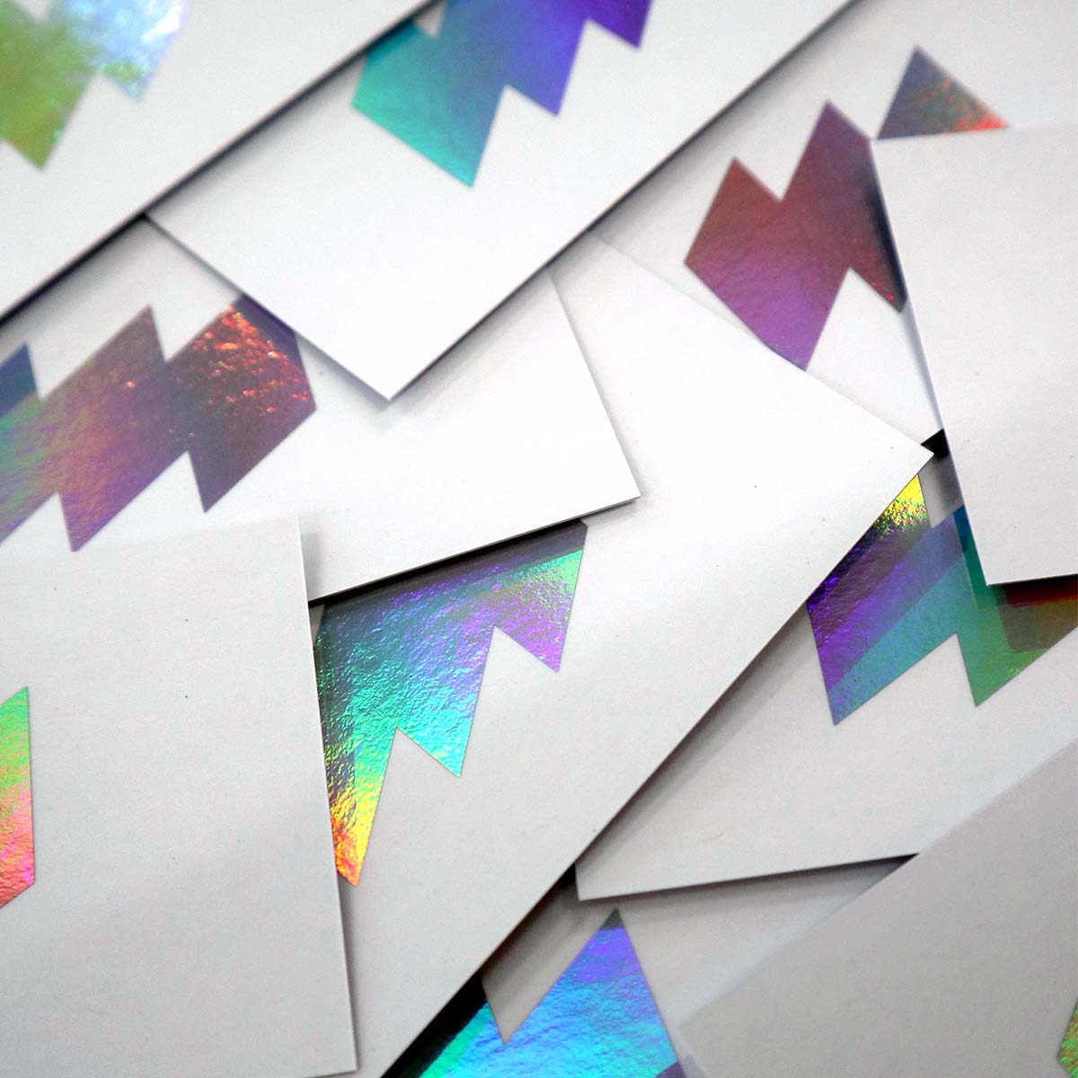 Close-up of stacked Business cards featuring a bold zigzag pattern printed in holographic foil on recycled paper with soft touch to front of the card