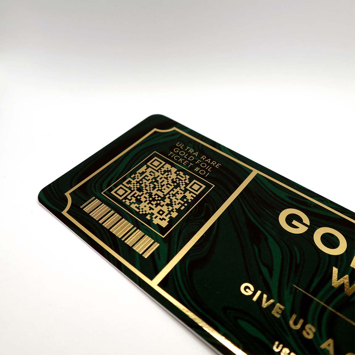 Close-up of a premium ticket printed on uncoated paper with metallic gold foil detailing on a dark green marbled background featuring a QR code with reflective foil accents